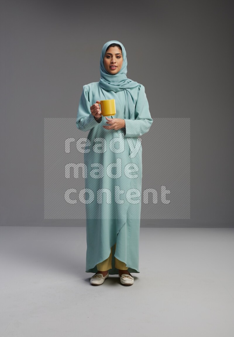 Saudi Woman wearing Abaya standing  holding a mug on Gray background
