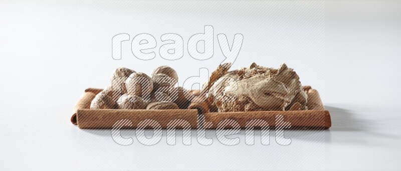 2 squares of cinnamon sticks full of dried ginger and nutmegs on white flooring