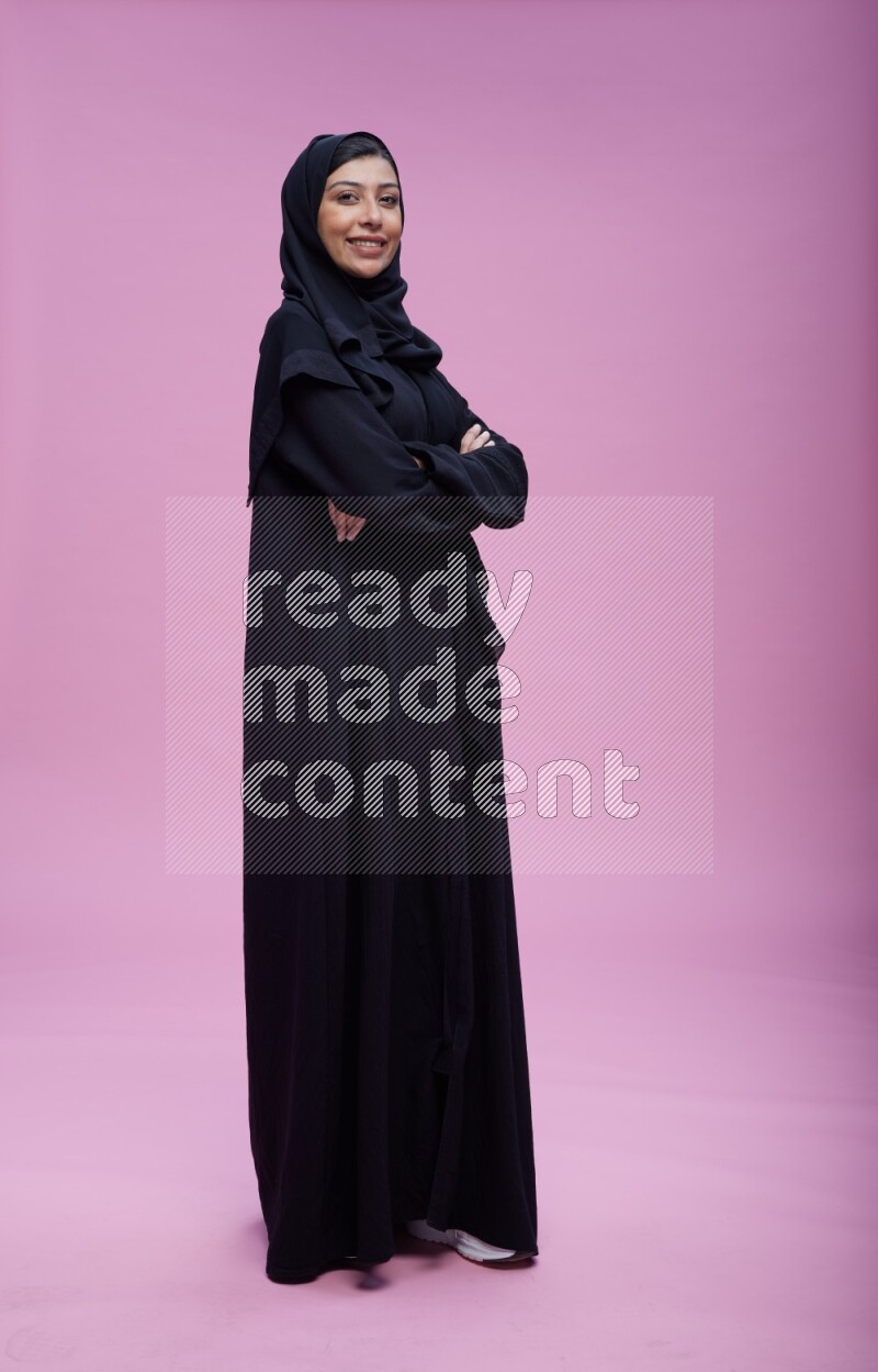 Saudi woman wearing Abaya standing with crossed arms on pink background