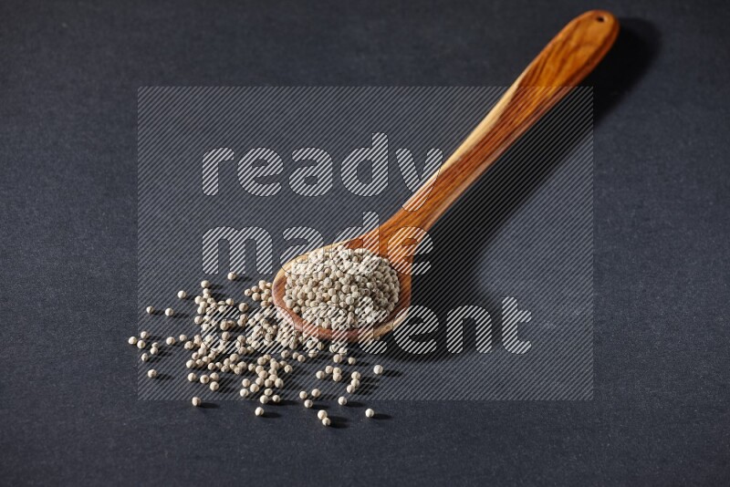 A wooden ladle full of white pepper beads on black flooring