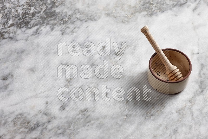 Beige Pottery oven bowl with wooden honey handle on the side with grey marble flooring, 65 degree angle