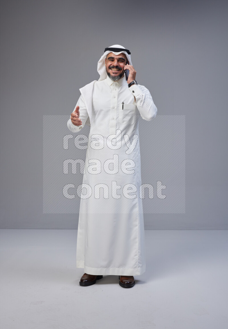 Saudi man Wearing Thob and white Shomag standing talking on phone on Gray background