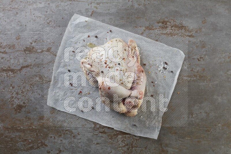 whole raw chicken on a parchment paper direct on a rustic grey background