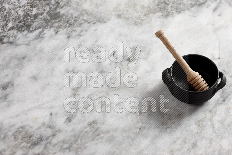 Black Pottery Bowl with wooden honey handle in it, on grey marble flooring, 65 degree angle