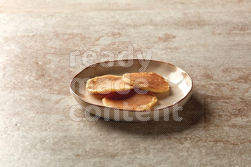 Three stacked plain mini pancakes in an irregular plate on beige background