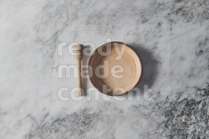 Beige pottery oven bowl with wooden honey dipper on the side on grey marble background