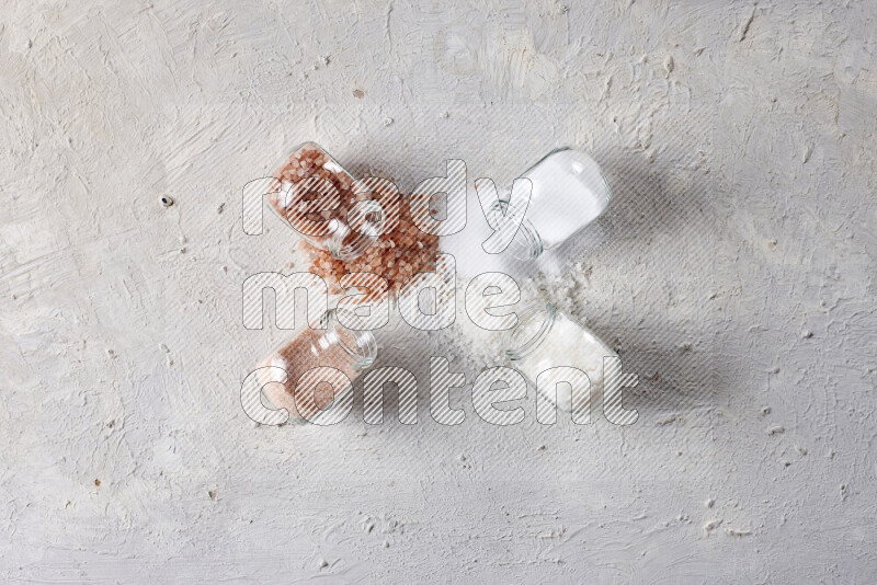 4 glass jars filled with table salt, coarse sea salt, fine himalayan salt and coarse himalayan salt on white background