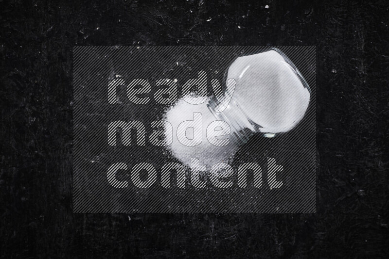 A glass jar full of fine table salt on black background