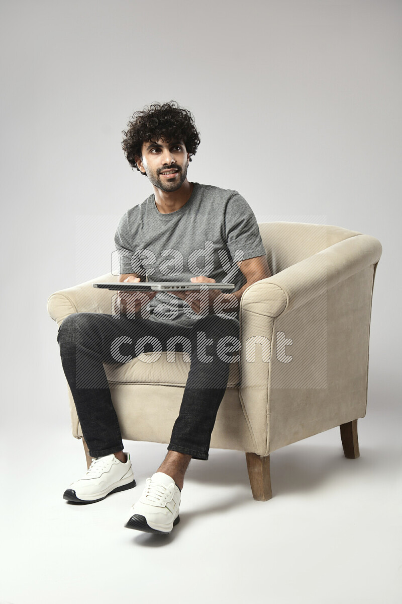 رجل يرتدي ملابس كاجوال يجلس علي كرسي و يحمل لاب توب علي خلفية بيضاء