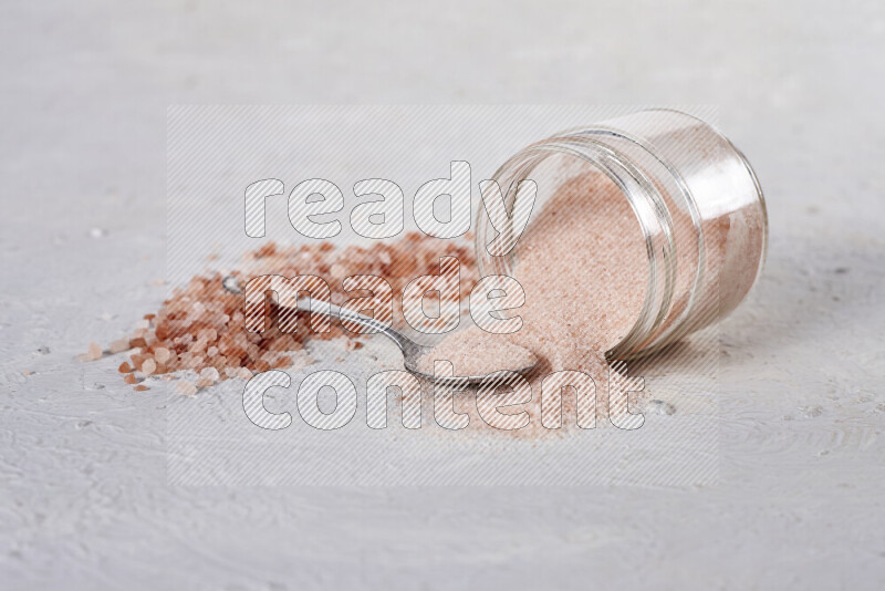 A glass jar full of fine himalayan salt with some himalayan crystals beside it on a white background