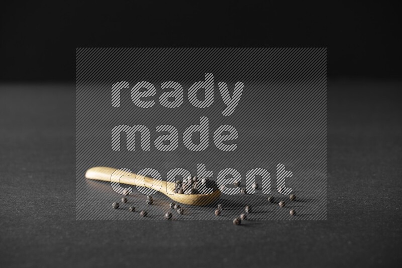 حبوب الفلفل الأسود في ملعقة خشبية علي خلفية سوداء