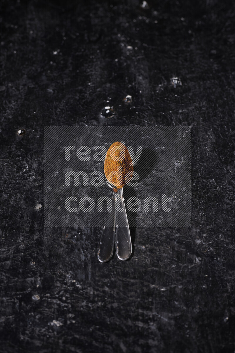 Two metal spoons full of ground paprika powder on black background