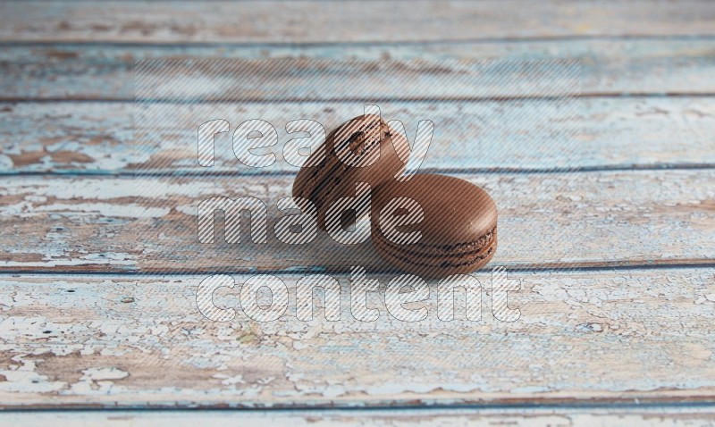 45º Shot of two Brown Dark Chocolate macarons on light blue wooden background