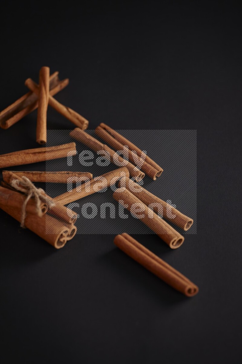 4 Cinnamon sticks stacked and bounded with more sticks in the background on black flooring