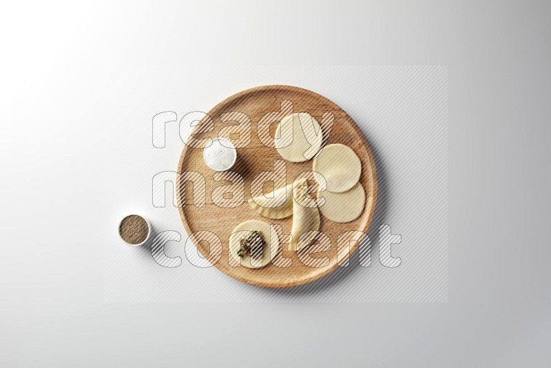 two closed sambosas and one open sambosa filled with meat while salt and black pepper aside in a wooden dish on a white background