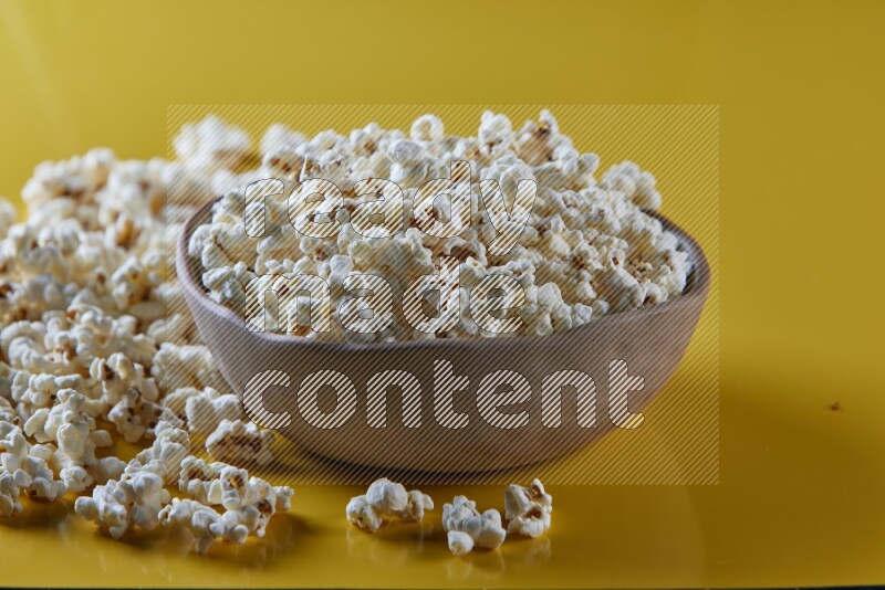 A brown pottery bowl full of popcorn with popcorn beside it on a yellow background in different angles