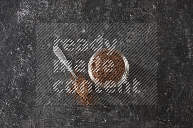 وعاء زجاجي ممتلئ ببودرة القرنفل مع ملعقة معدنية على أرضية سوداء