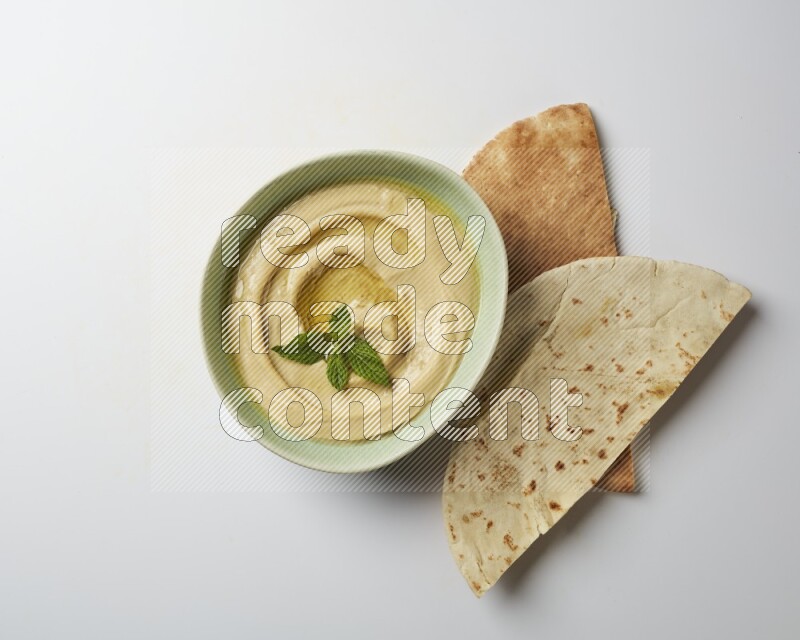 Hummus in a green plate garnished with mint on a white background