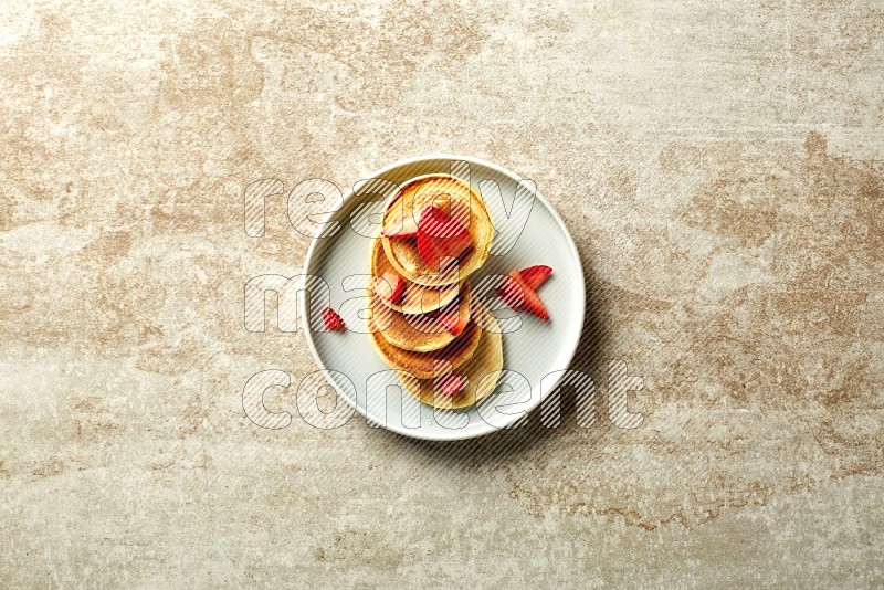 Five stacked strawberry mini pancakes in a blue plate on beige background
