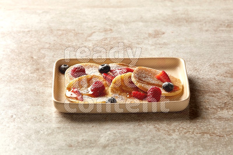 Five stacked mixed berries mini pancakes in a rectangular plate on beige background
