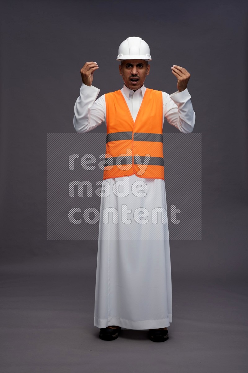 Saudi man wearing thob with engineer vest standing interacting with the camera on gray background