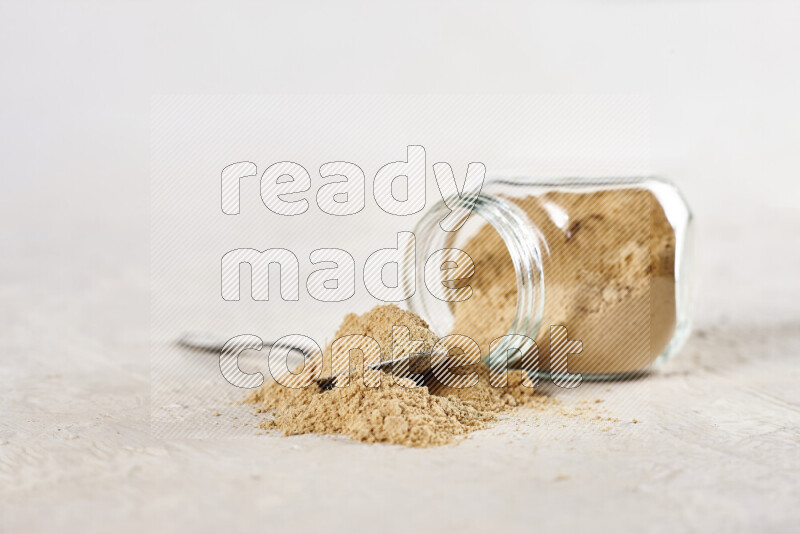 A glass jar full of ground ginger powder flipped with some spilling powder on white background