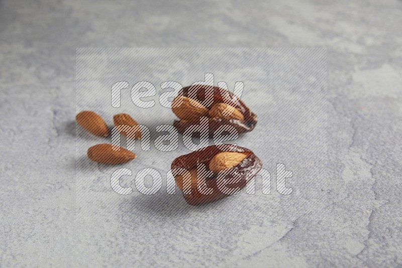 two Almond stuffed date with unroasted  almonds on a light grey background