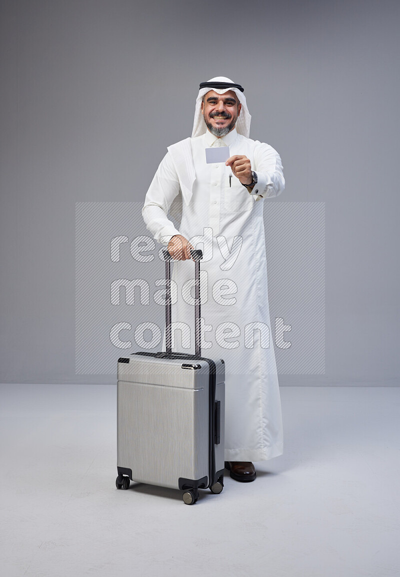 رجل سعودي يرتدي ثوب ابيض ويحمل بطاقة بنكية وبجواره حقيبة سفر