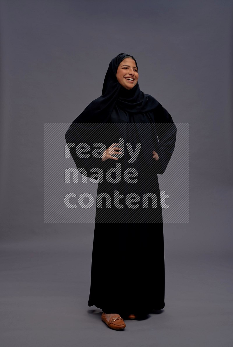 Saudi woman wearing Abaya standing interacting with the camera on gray background