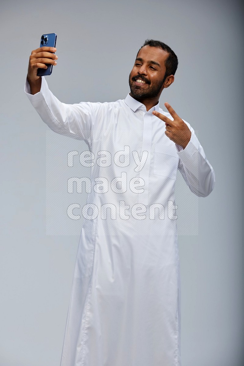 Saudi man wearing Thob standing taking selfie on Gray background