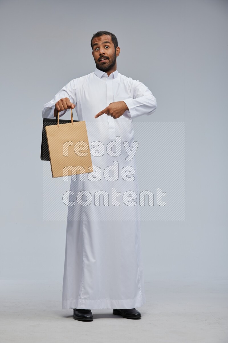 Saudi man Wearing thob standing holding shopping bag on Gray background