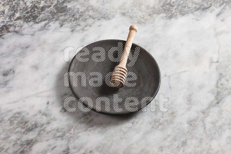 Black Pottery Plate with wooden honey handle in it, on grey marble flooring, 65 degree angle
