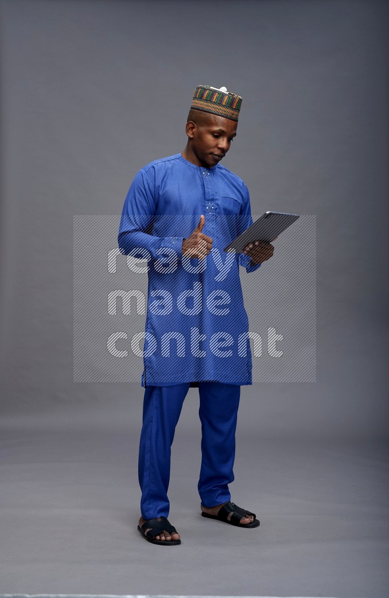 Man wearing Nigerian outfit standing working on tablet on gray background
