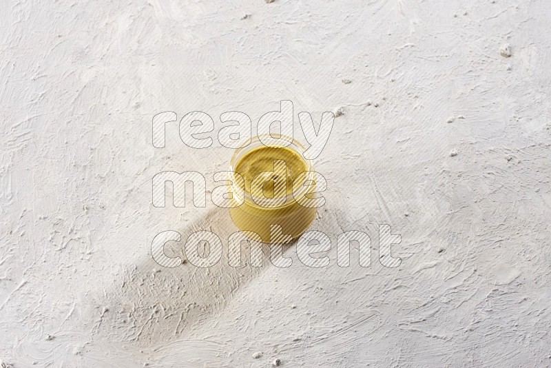 A glass jar full of mustard paste on a textured white flooring