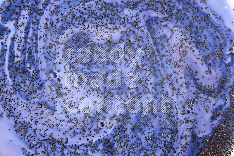 A close-up of sparkling gold glitter scattered on swirling blue background