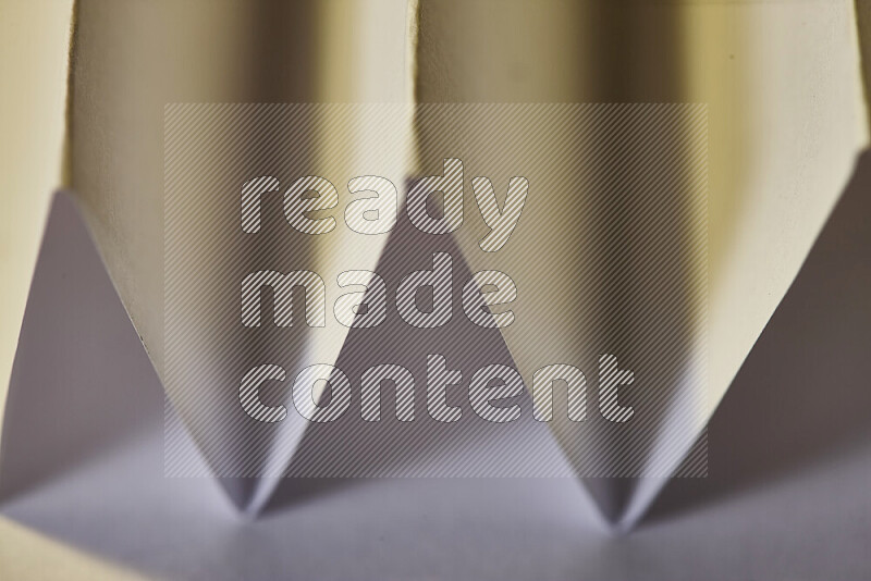 A close-up abstract image showing sharp geometric paper folds in white gradients and warm tones