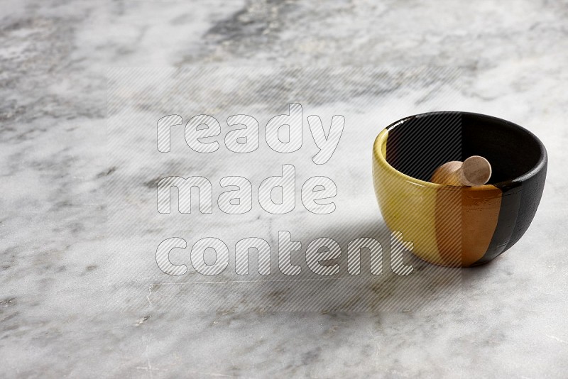 Multicolored Pottery bowl with wooden honey handle in it, on grey marble flooring, 45 degree angle