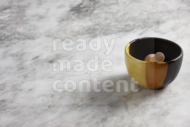Multicolored pottery bowl with wooden honey dipper in it on grey marble background