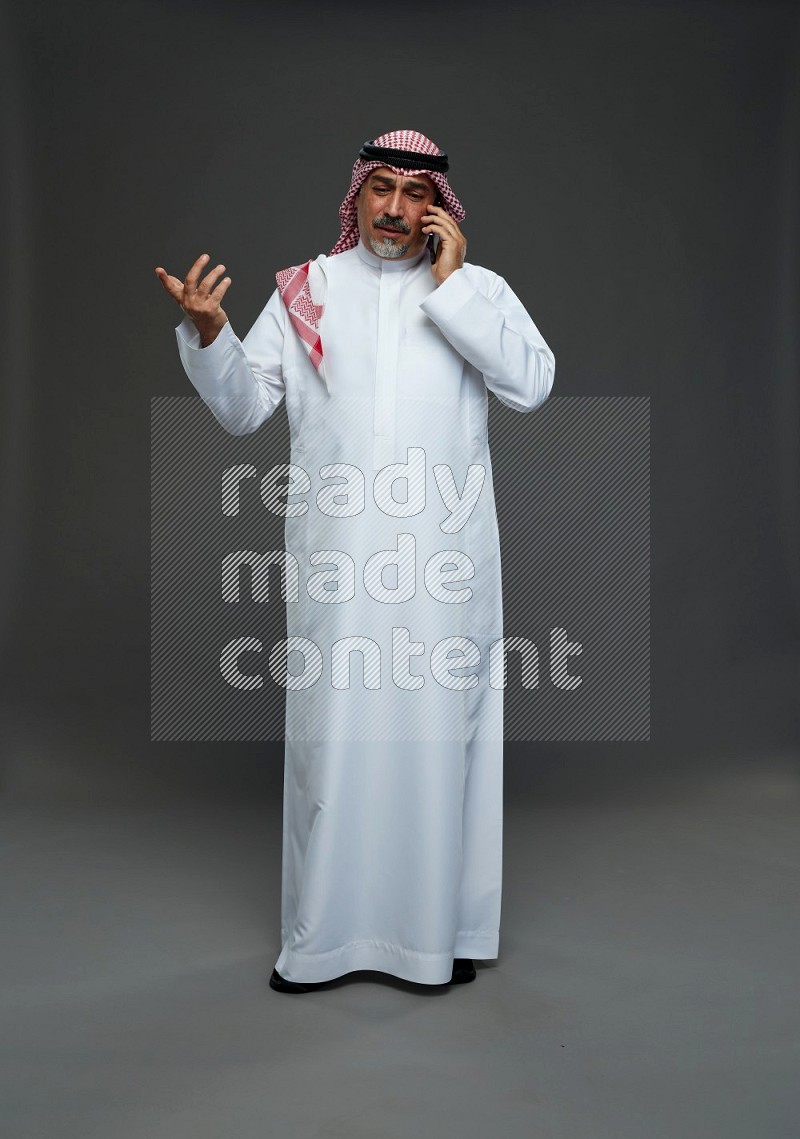 Saudi man with shomag Standing talking on phone on gray background