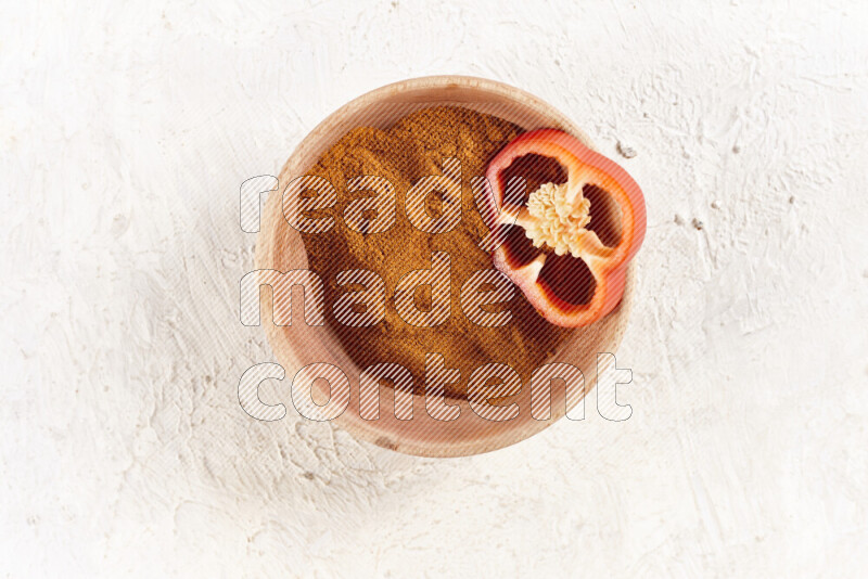 A wooden bowl full of ground paprika powder on white background