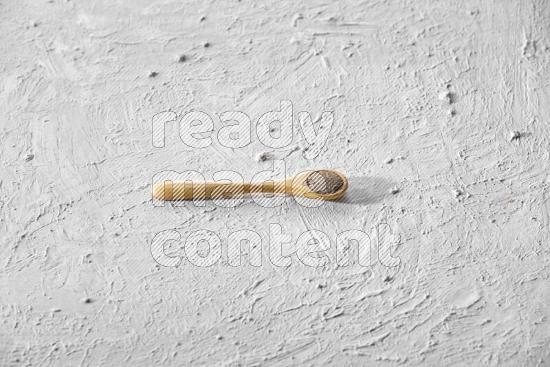 A wooden spoon full of black pepper powder on a textured white flooring