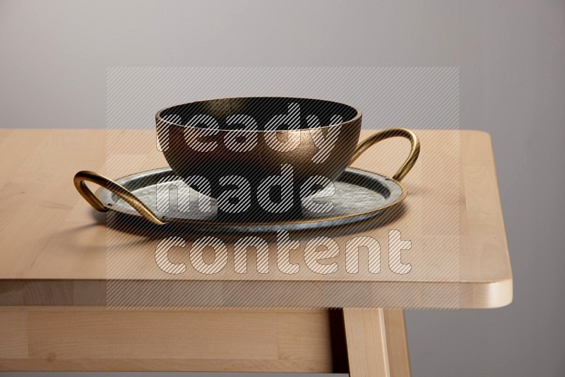 brass bowl placed on a rounded stainless steel metal tray with golden handels on the edge of wooden table