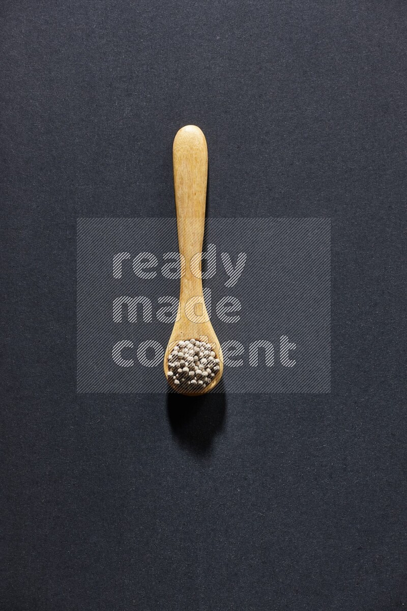 A wooden spoon full of white pepper beads on black flooring