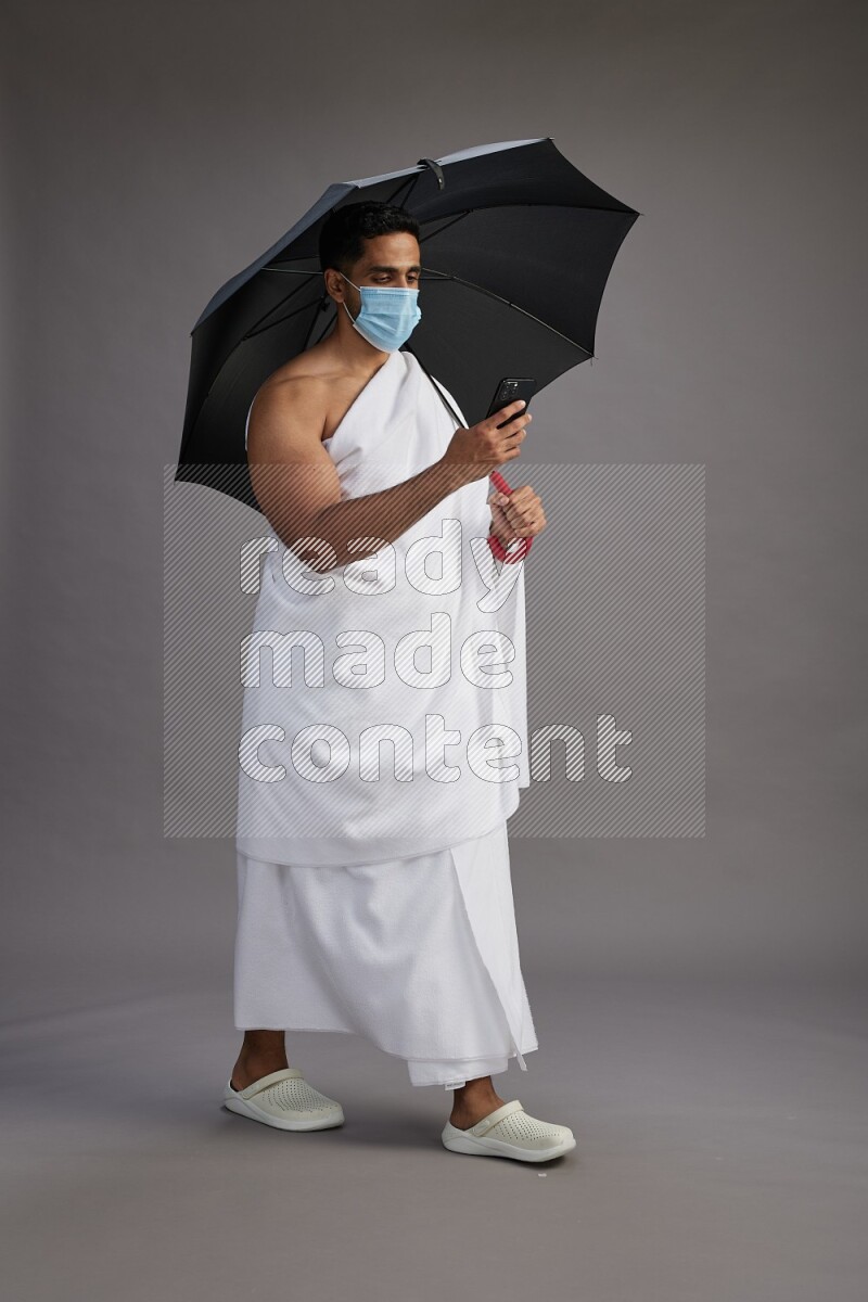 A man wearing Ehram and mask Standing holding umbrella on gray background on gray background