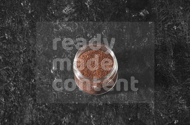 A glass jar full of garden cress seeds on a textured black flooring