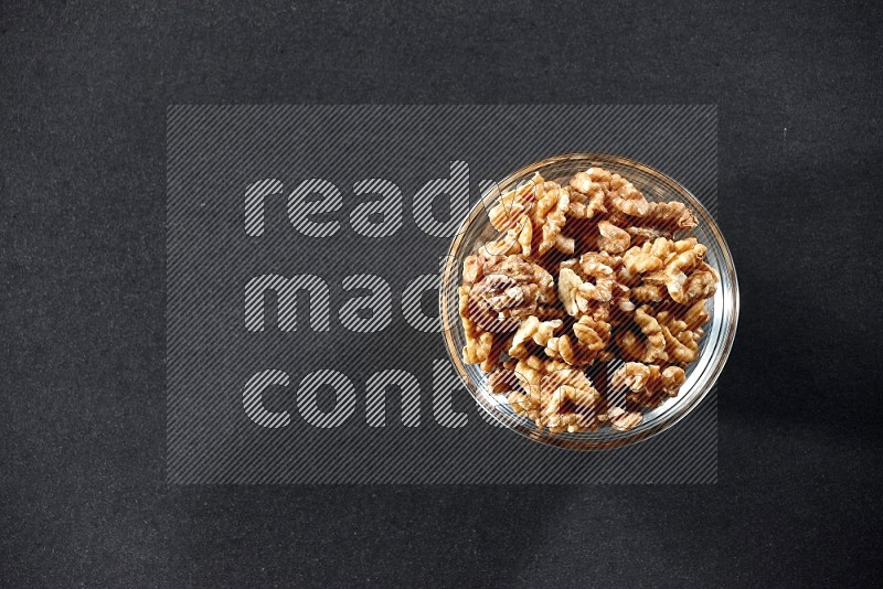 A glass bowl full of peeled walnuts on a black background in different angles