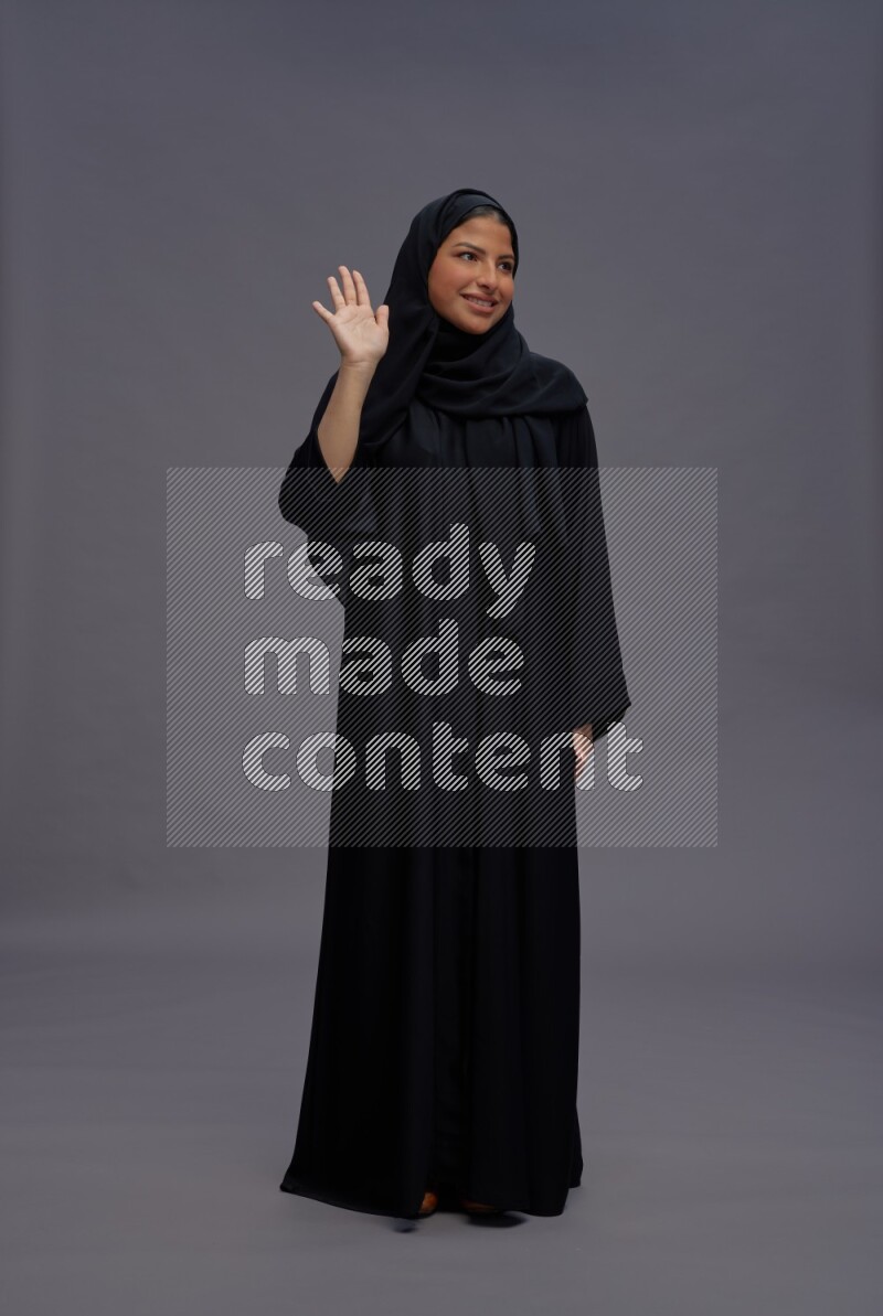 Saudi woman wearing Abaya standing interacting with the camera on gray background