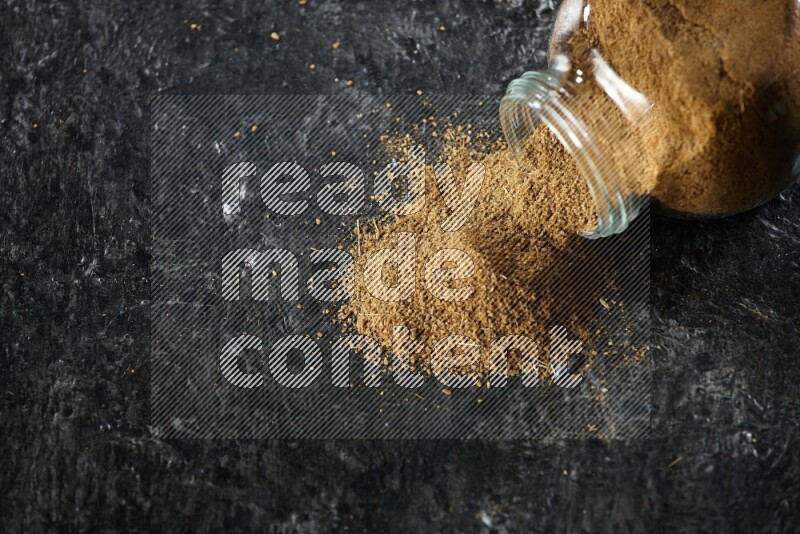 وعاء زجاجي مقلوب ممتلئ ببودرة الكمون والبودرة تناثرت منه على خلفية سوداء