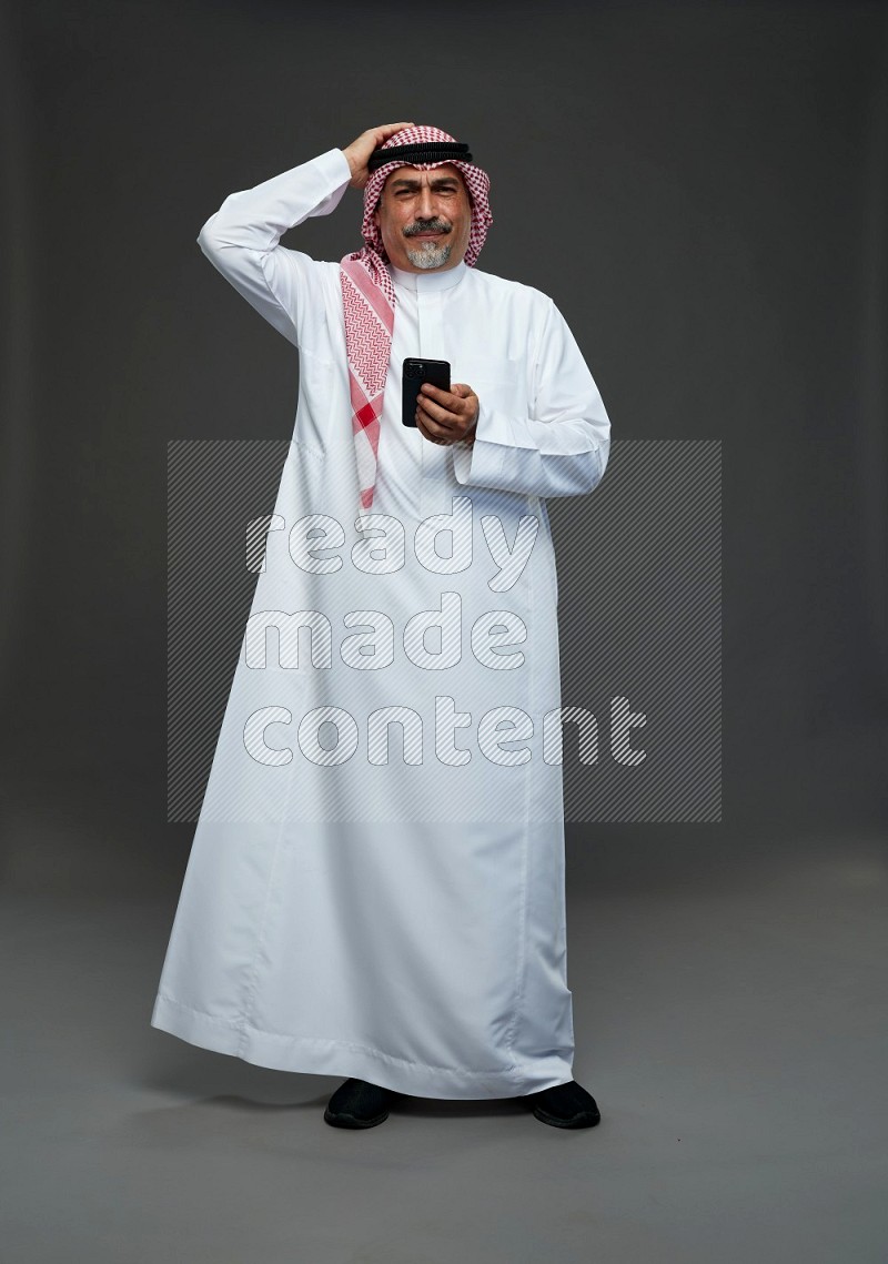 Saudi man with shomag Standing texting on phone on gray background