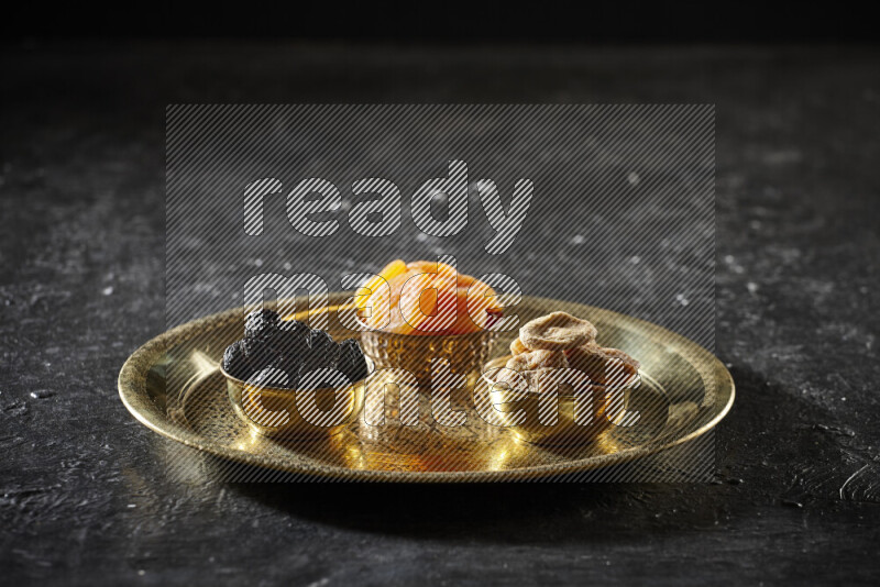 Dried fruits in metal bowls on a tray in a dark setup